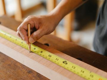 Vermessung eines Holzbalkens mit einem gelben Maßband